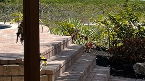 Un poste de madera con una farola, escaleras que llevan a una piscina y vistas al océano y vegetación.