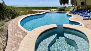 Una piscina con un jacuzzi, rodeada de sillones de descanso y vistas al océano.
