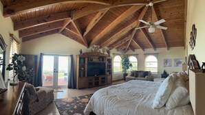 Una habitación amplia con alto techo de madera, una cama grande, televisión y un balcón con puertas correderas.