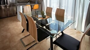 Una cucina moderna con zona pranzo, caratterizzata da un tavolo in vetro, sedie in legno e un frigorifero.