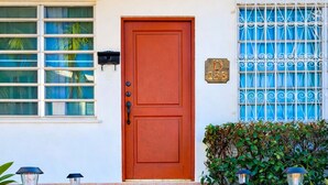 Una escalera de piedra que lleva a una puerta roja, con un buzón y una ventana con barrotes azules.
