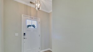 Un couloir avec une porte blanche, un luminaire au plafond et une petite fenêtre donnant sur des arbres.