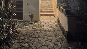 A stone-paved courtyard with a wooden staircase leading to a door, surrounded by potted plants and a stone wall. - In the heart of Tuscany, beautiful garden with swimming pool, Casa di Ele awaits you (Gambassi Terme Firenze)