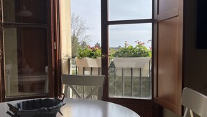 A round table with a basket, a chair, and a view through a large window to a balcony with plants. - In the heart of Tuscany, beautiful garden with swimming pool, Casa di Ele awaits you (Gambassi Terme Firenze)