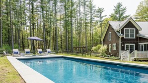 Piscina com espreguiçadeiras e deck, cercada por uma floresta.