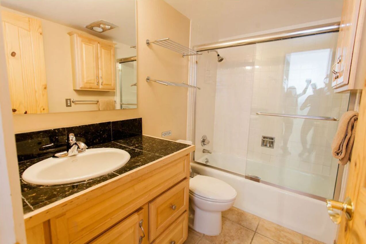 A bathroom with a sink, vanity, mirror, toilet, and a glass-enclosed shower area.