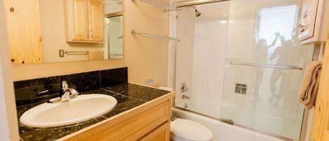 A bathroom with a sink, vanity, mirror, toilet, and a glass-enclosed shower area.
