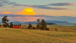A rural landscape with a red house, a dirt path, and a clear sky with clouds.