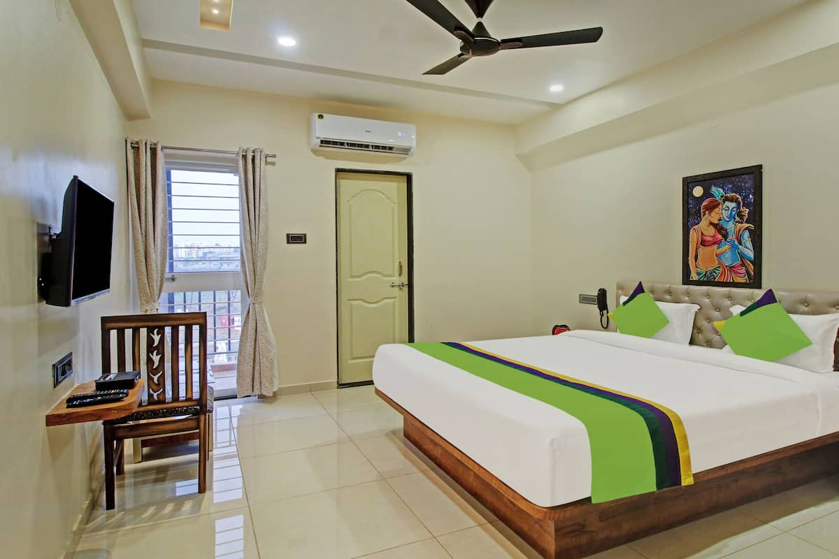 A hotel room with a bed, a television, a desk, and a window with curtains.