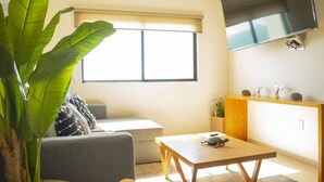 Ein modernes Wohnzimmer mit einem grauen Sofa, einem Holztisch und einer großen Zimmerpflanze.