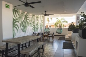 Relax in a serene outdoor space with a long bench, chairs, and a hanging chair, surrounded by lush foliage and a mural.