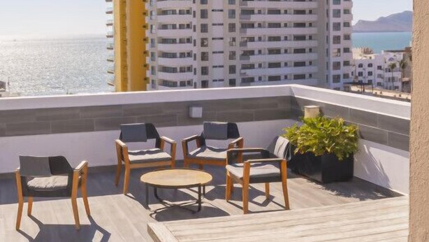 Eine Dachterrasse mit Gartenmöbeln, Blick auf das Meer und ein Hochhaus im Hintergrund.
