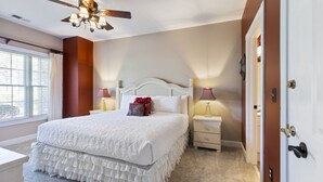Une chambre à coucher avec un grand lit, deux tables de chevet, un ventilateur de plafond et une porte.