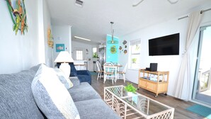 A living room with a grey sofa, a glass coffee table, and a TV on the wall.