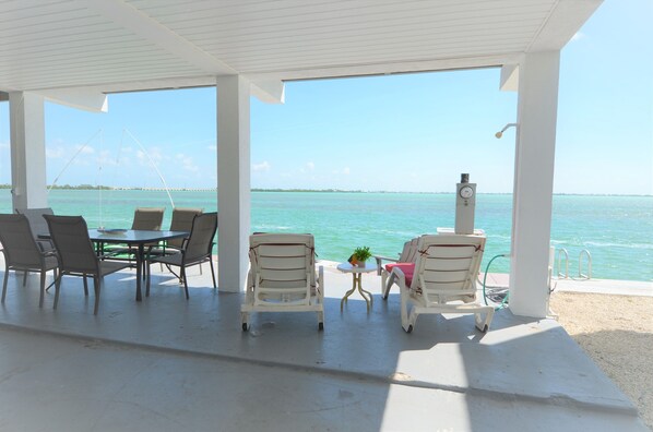 A covered outdoor seating area with a table and chairs, overlooking a body of water.