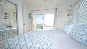 A bedroom with a bed, a wardrobe, a mirror, a door, and a view of the sea through a balcony.