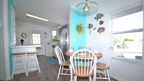 A modern kitchen with white cabinets, a wooden dining table with four chairs, and a large window providing a view of the outside.