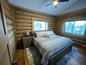 Un dormitorio tipo cabaña de madera con una cama, mesitas de noche y un ventilador de techo.