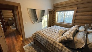 A log cabin bedroom with a large bed, a window with a view of trees, and a hammock hanging on the wall. - Best Mtn/Lake views!!! Lodge on esteemed Lakeside Drive! Hot tub! Fido friendly! (Grand Lake)