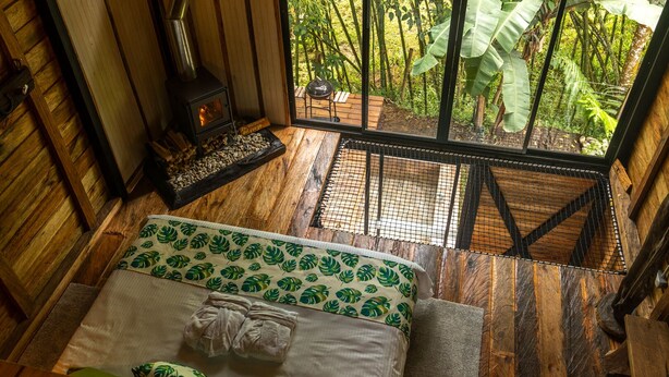 A wooden room with a bed, a fireplace, and a view of a lush garden. - Glamping Lagos de Venecia (Santa Rosa de Cabal)