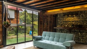 A modern living room with a light blue sofa, a stone wall, and a large window overlooking a garden. - Glamping Lagos de Venecia (Santa Rosa de Cabal)