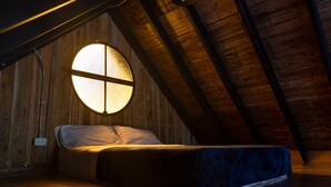 A cozy attic bedroom with a bed, a circular window, wooden beams, and a sloped ceiling. - Glamping Lagos de Venecia (Santa Rosa de Cabal)
