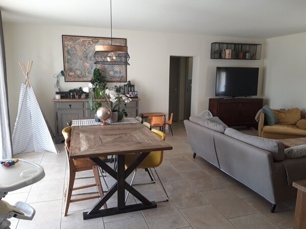 A living room with a sofa, a dining table with chairs, a kitchen area with a globe and plants, and a television.