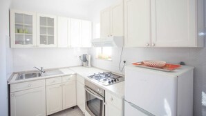 A compact kitchen with white cabinets, a gas stove, a built-in oven, and a refrigerator. - AGATA Two-Bedroom Apartment 5 (Banjole)