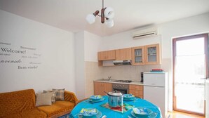 A cozy living room with a sofa and a dining table set for four, a kitchen with wooden cabinets and a built-in oven, and a large window providing natural light. - AGATA Two-Bedroom Apartment 6 (Banjole)