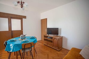 A small, well-lit room with a dining table set for two, a television on a wooden stand, and a sofa. - AGATA Two-Bedroom Apartment 6 (Banjole)