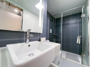 A modern bathroom with a large white sink, a glass shower enclosure, and a mirror above the sink.