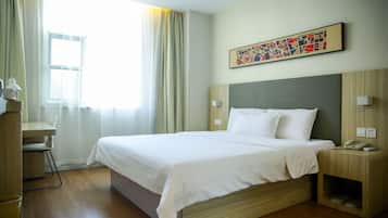 A hotel room with a bed, bedside table, lamp, and a painting on the wall.