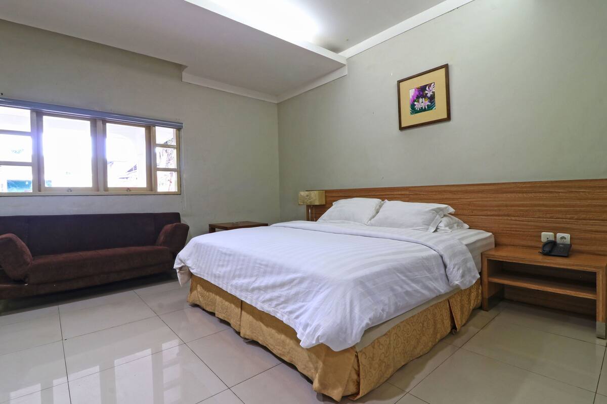 Una habitación de hotel con una cama grande, un sofá, una mesita de noche y una ventana con persianas.