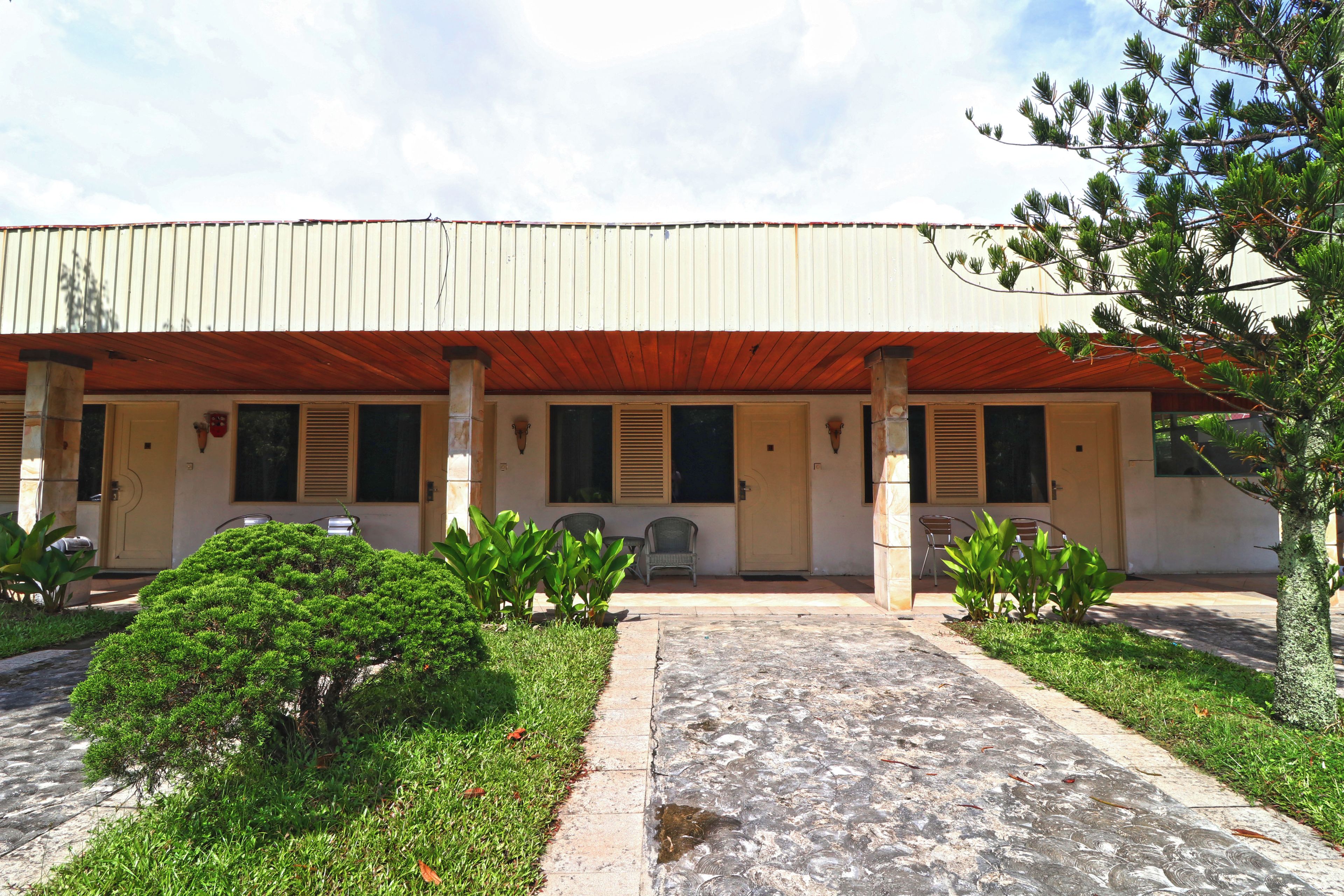 A building with a covered porch, potted plants, and a paved walkway.