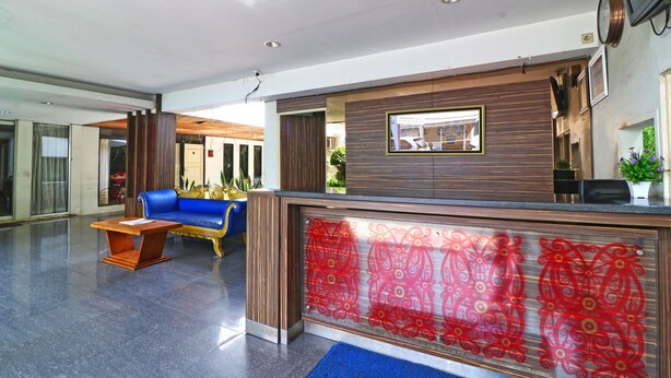 A reception area with a blue sofa, a wooden reception desk, and a red patterned glass partition. - Hotel Sampaga by Zuzu (Banjarmasin)