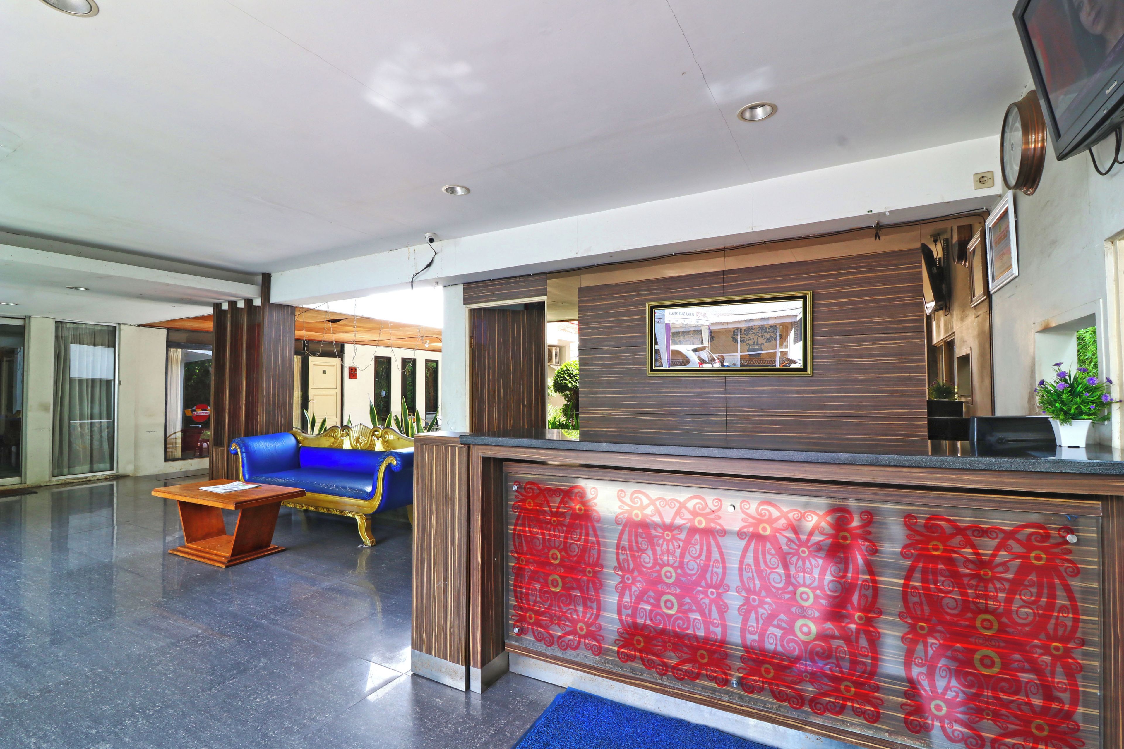A reception area with a blue sofa, a wooden reception desk, and a red patterned glass partition.