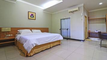 A hotel room with a bed, a desk, a chair, a window with curtains, and a door.