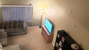 A living room with a sofa, a coffee table, a TV on a wooden stand, a bookshelf, and a ceiling fan.