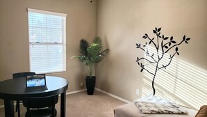 A room with a round table, a laptop, a potted plant, a sofa, and a wall decoration.