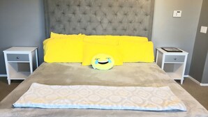 A bedroom with a tufted headboard, two bedside tables, a bed with a patterned duvet, and a pillow with a smiling face.