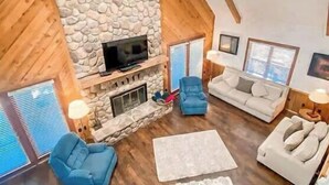 A spacious living room with a stone fireplace, wooden beams, and a high ceiling.
