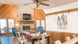 A spacious dining area with a stone fireplace, wooden ceiling, and a large table surrounded by chairs.