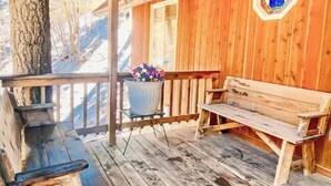A wooden deck with a bench and a table, a potted plant, and a hexagonal stained glass window.