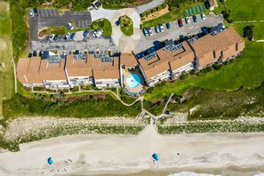An aerial view of a resort with a swimming pool, parking area, and beachfront.