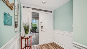 Um corredor com piso de madeira, porta branca e vista para o exterior.