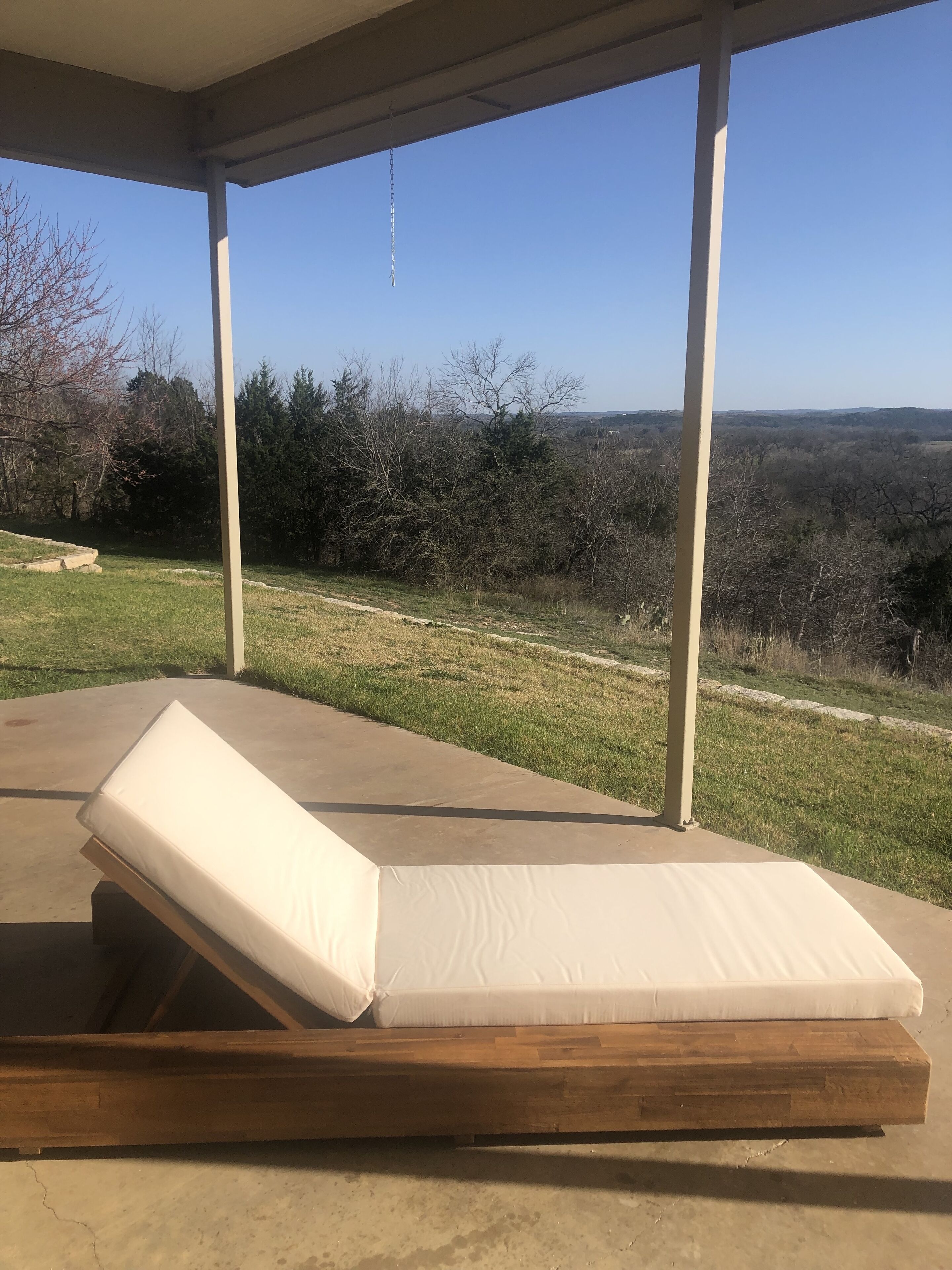A covered outdoor seating area with a wooden bench and a mattress.