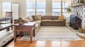 Una sala de estar acogedora con chimenea de piedra, una mesa de centro de madera y un amplio ventanal con vistas a la ciudad.