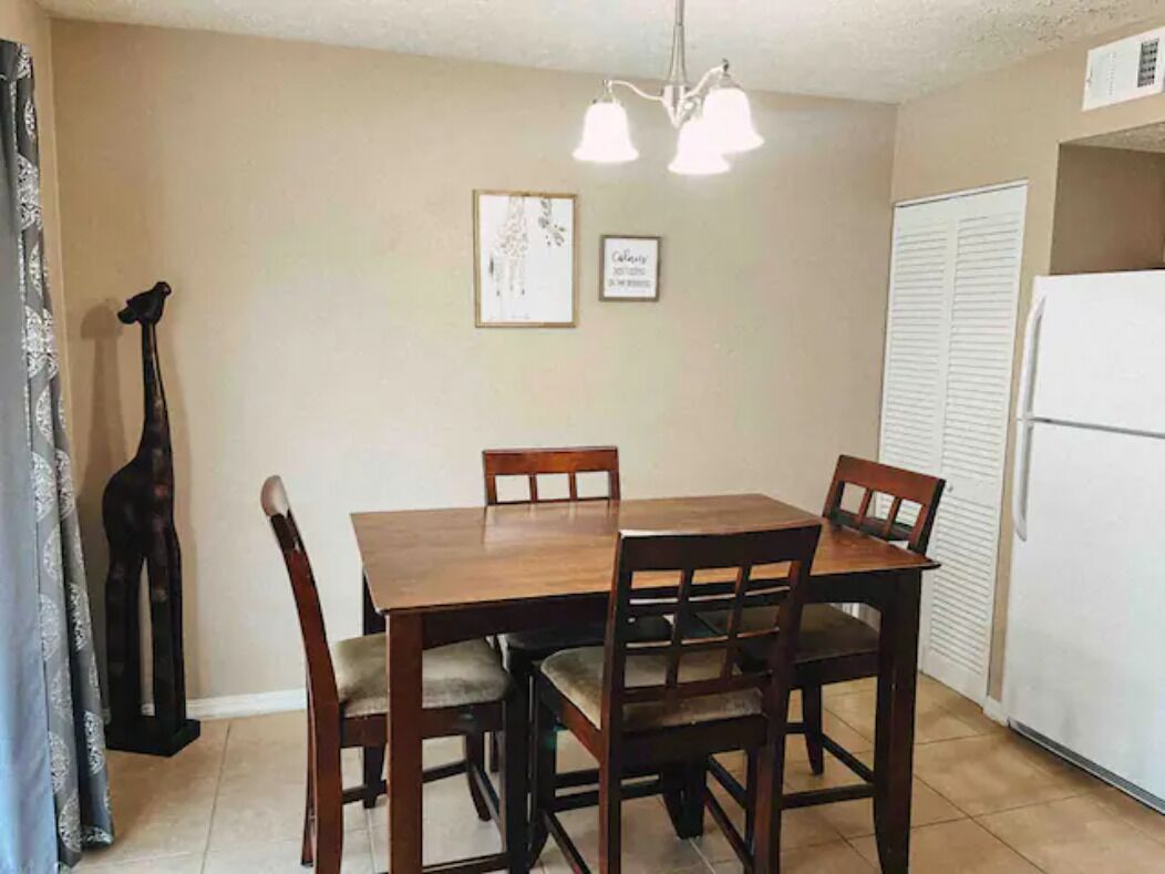 Un comedor con mesa y sillas de madera, una araña, obras de arte enmarcadas en la pared y un refrigerador al fondo.