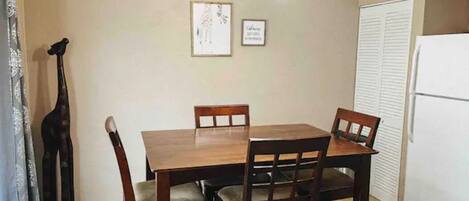 Un comedor con mesa y sillas de madera, una araña, obras de arte enmarcadas en la pared y un refrigerador al fondo.