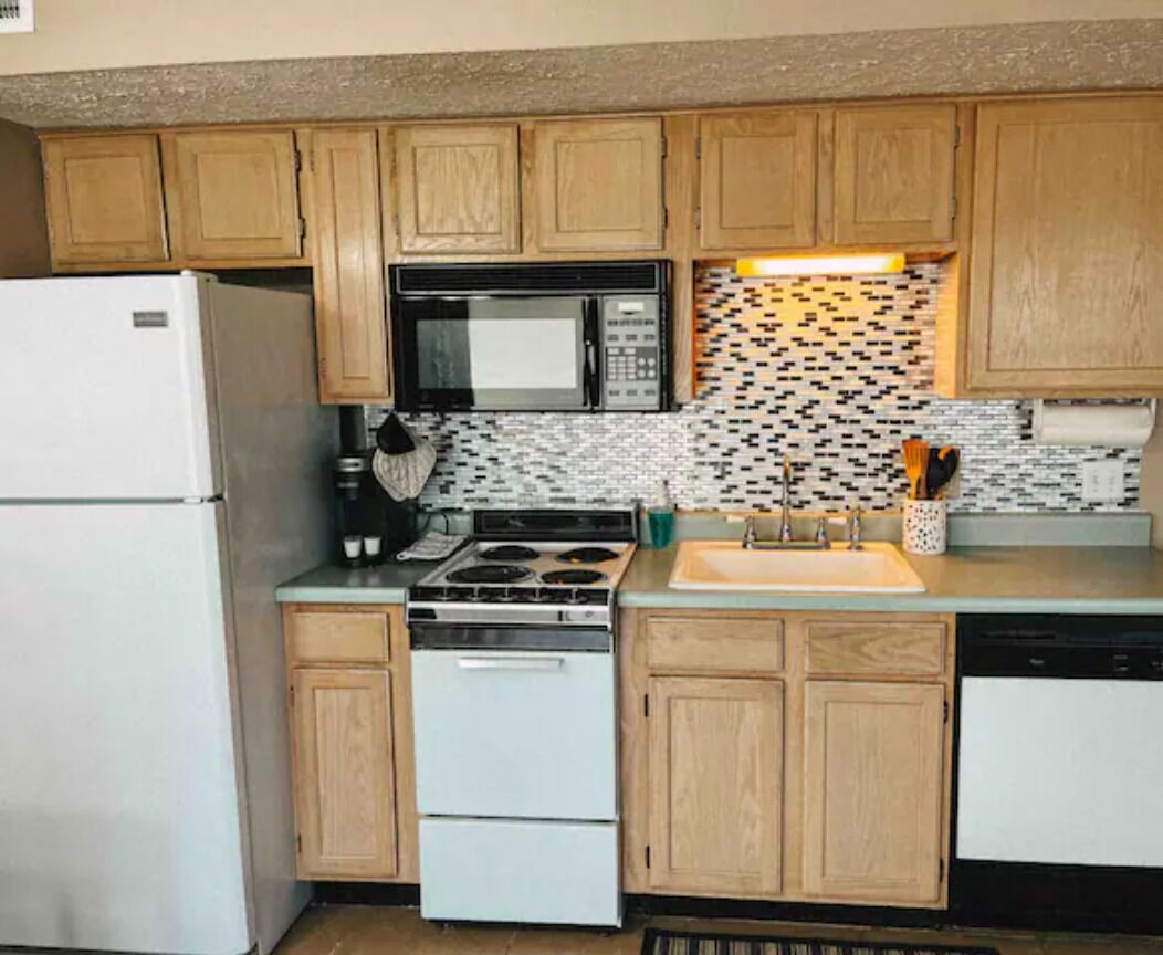 A compact kitchen with wooden cabinets, a white refrigerator, a microwave, a stove, and a sink.